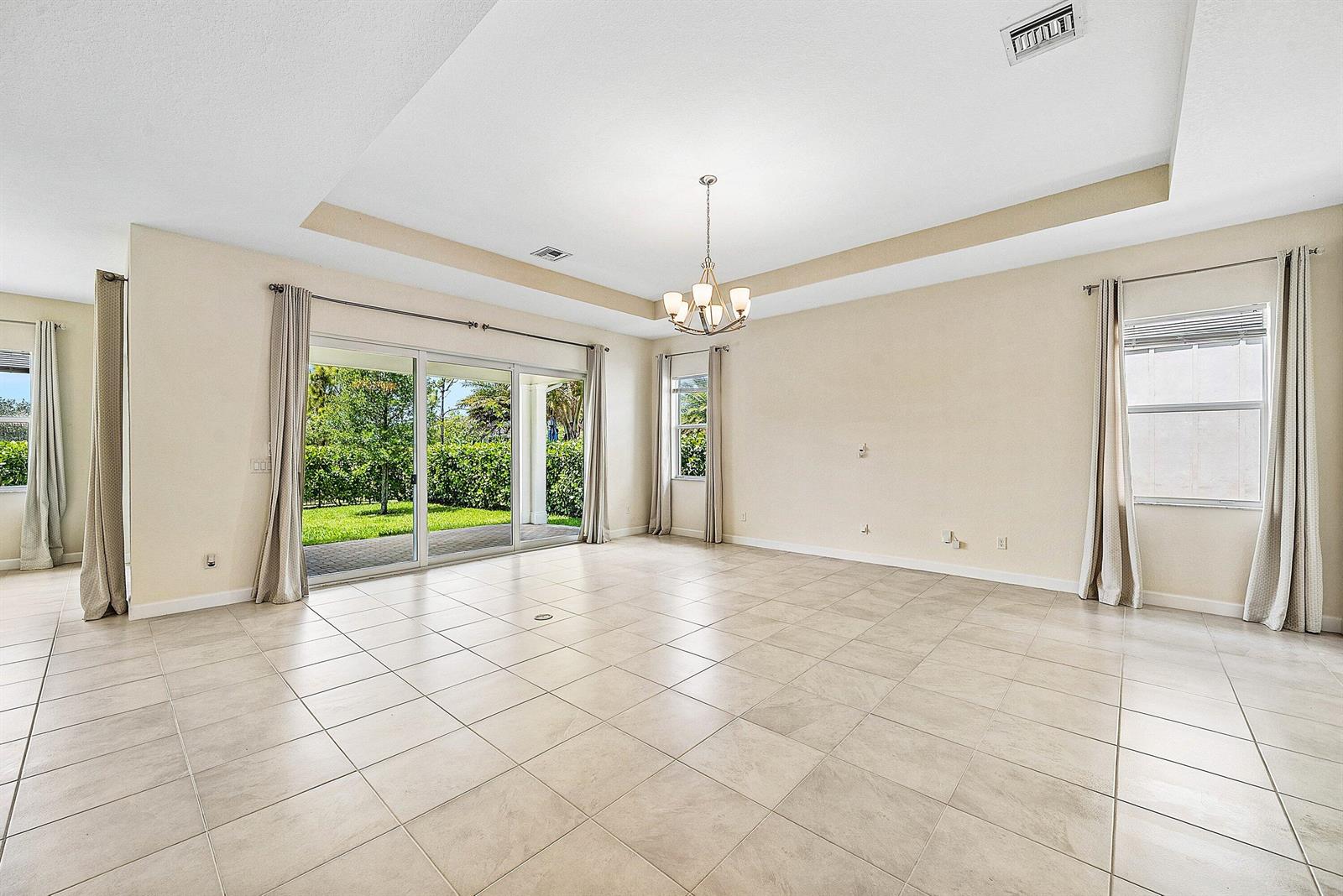 An empty living room features beige tile floors, a tray ceiling, and sliding glass doors — 1031 Ember Ridge Run, Loxahatchee FL 33470, LOXAHATCHEE, FL