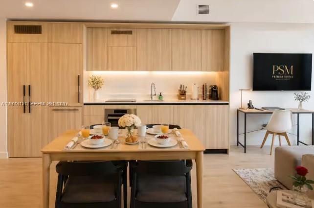 A modern kitchen with light wood cabinetry and a dining table sits next to a desk — 225 N Miami Ave # 3204, Miami FL 33128, MIAMI, FL