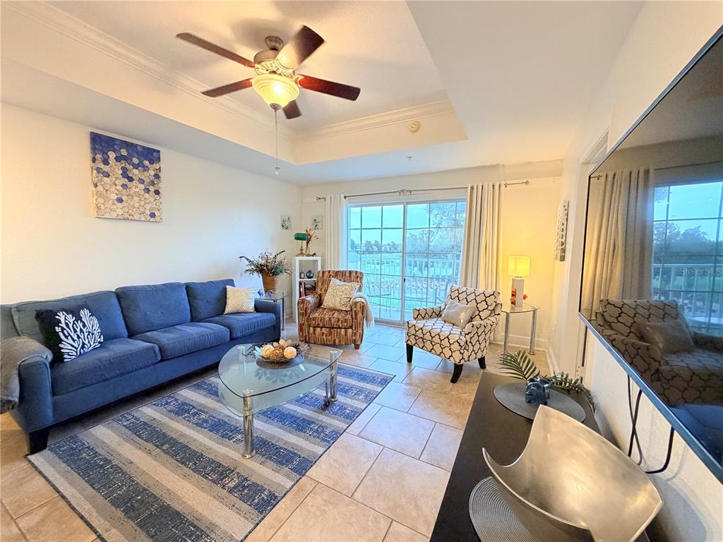 A living room features a blue sofa, patterned armchairs, a glass coffee table, and tile flooring — 1323 SEVEN EAGLES COURT UNIT 202, REUNION, FL