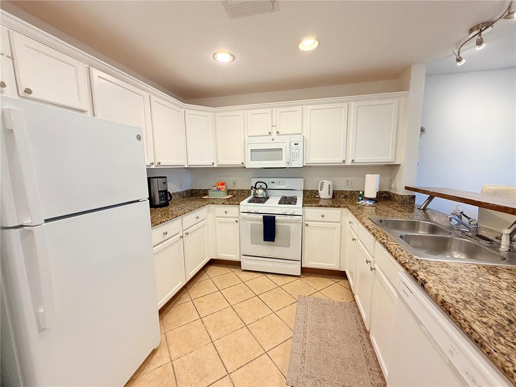 A kitchen features white cabinets, granite countertops, a white refrigerator, and a tiled floor — 1323 SEVEN EAGLES COURT UNIT 202, REUNION, FL