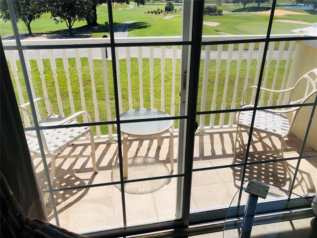 A view through a glass sliding door shows a balcony with two chairs and table — 1323 SEVEN EAGLES COURT UNIT 202, REUNION, FL