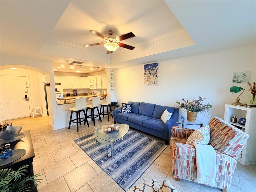 A living room with a blue sofa, patterned armchair, and an open kitchen with bar seating — 1323 SEVEN EAGLES COURT UNIT 202, REUNION, FL