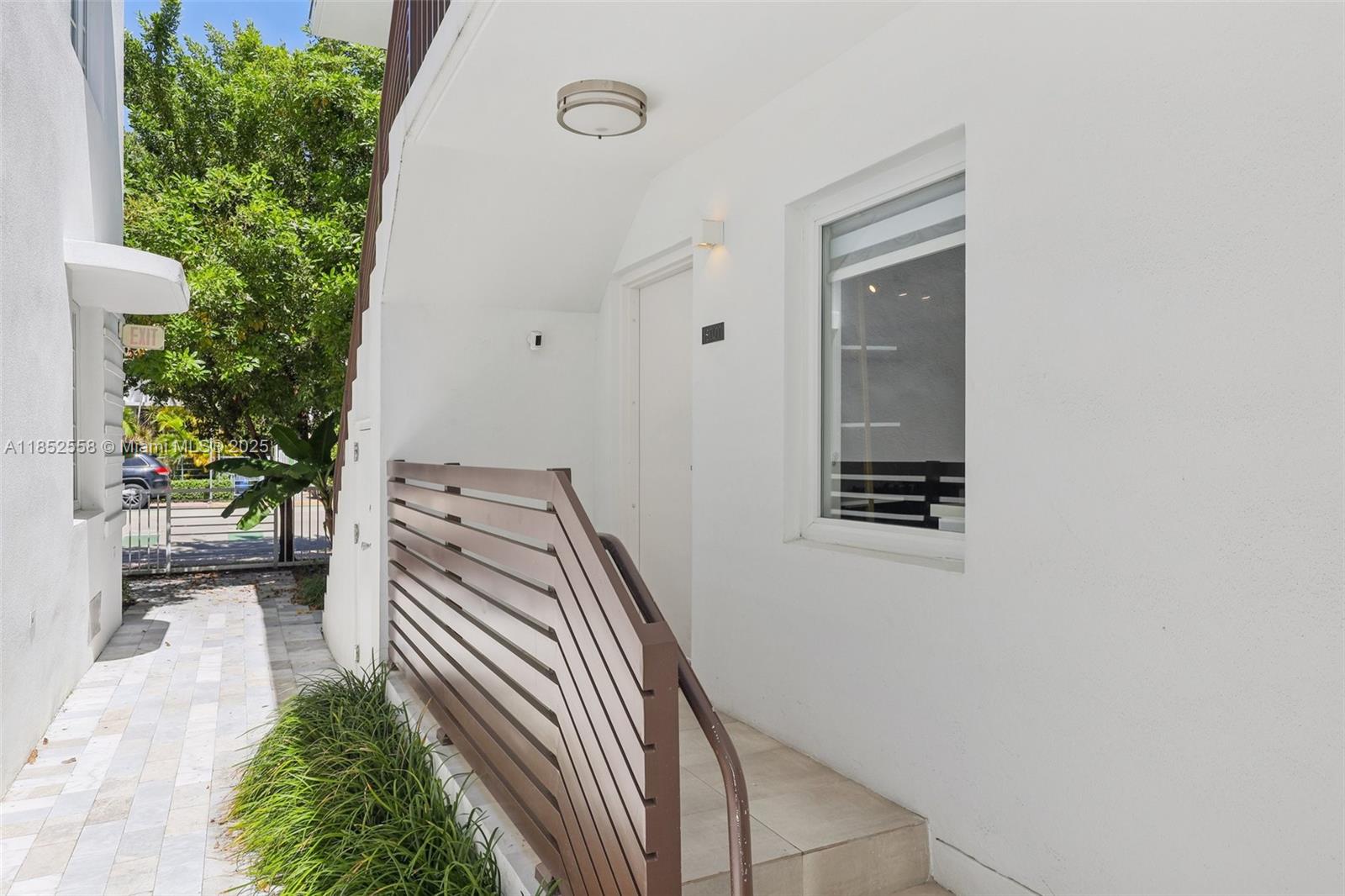An exterior view of a building entrance with a brown slatted railing and stairs — 1610 Euclid Ave # B101, Miami Beach FL 33139, MIAMI BEACH, FL