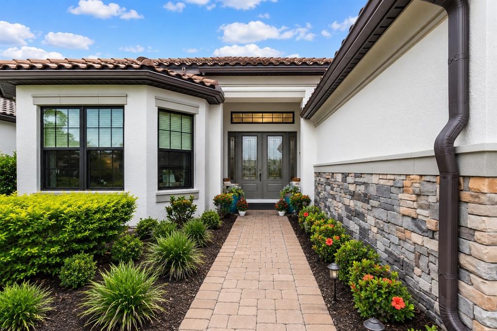 A stone-accented house exterior features a paved walkway leading to a double-door entryway — 10342 MORNING MIST LANE, SARASOTA, FL
