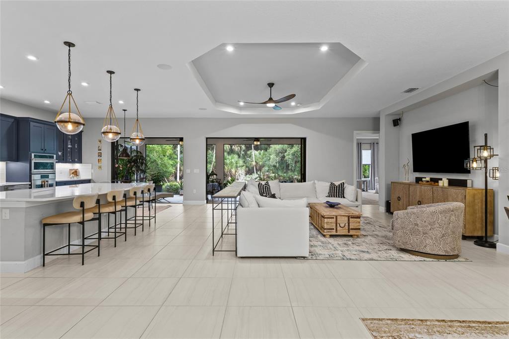 An open-concept living room and kitchen feature a tray ceiling, tile floors, and sliding doors — 10342 MORNING MIST LANE, SARASOTA, FL