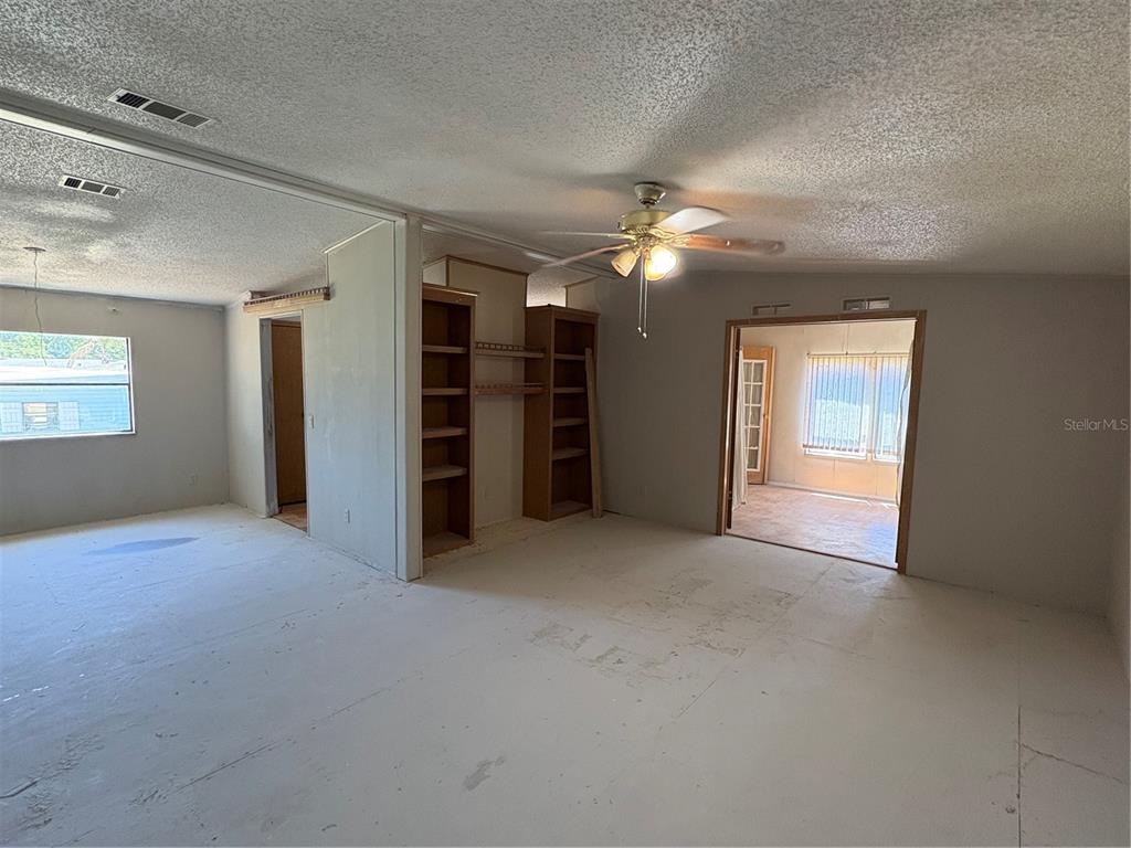 An interior view of a living area with unfinished flooring, built-in shelves, and a ceiling fan — 25034 BETTON HILL, LEESBURG, FL