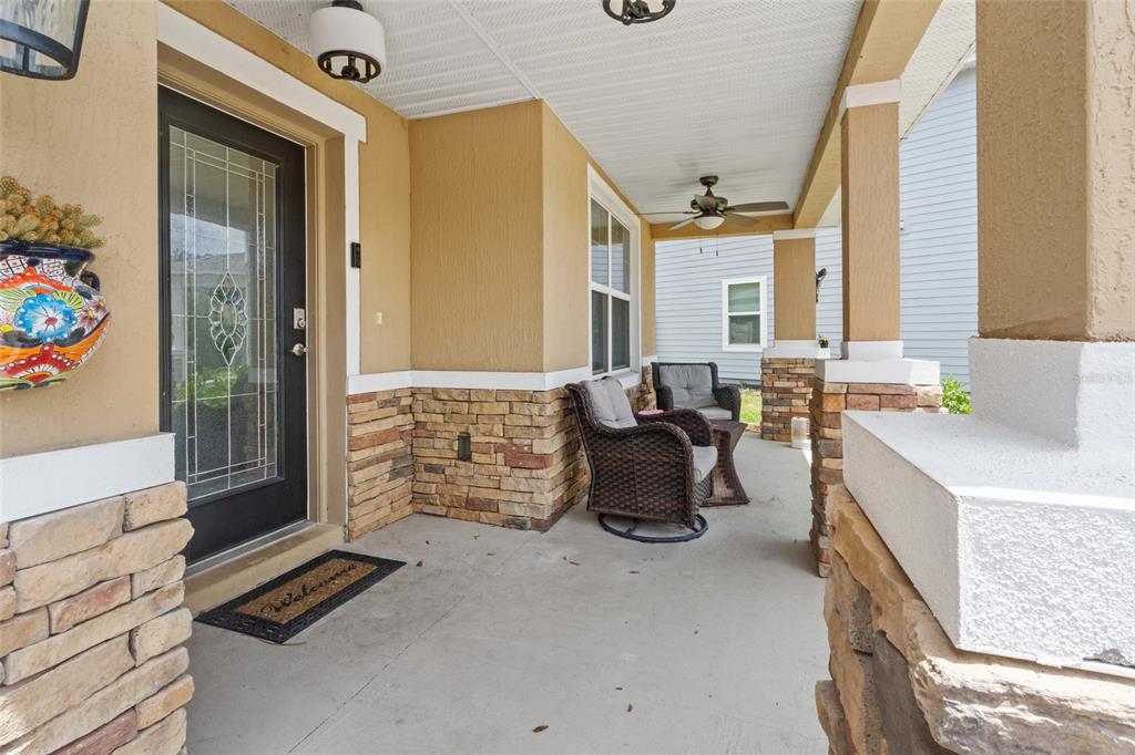 A covered front porch features stone accents, a dark front door, and outdoor wicker furniture — 672 NW 247TH TERR, NEWBERRY, FL