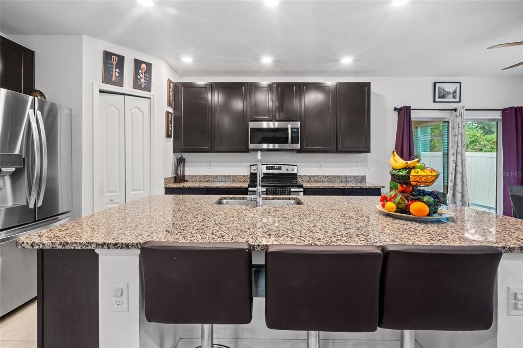 A kitchen features dark wood cabinets, granite countertops, a central island, and stainless steel appliances — 672 NW 247TH TERR, NEWBERRY, FL