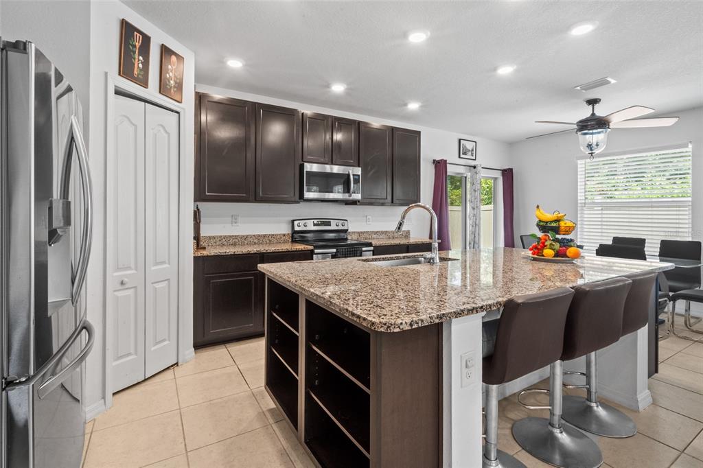 A kitchen features dark wood cabinets, granite countertops, a center island, and stainless steel appliances — 672 NW 247TH TERR, NEWBERRY, FL