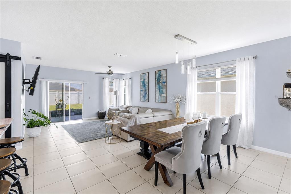 An open-concept living and dining area with light blue walls, tile floors, and large windows — 1795 PARTIN TERRACE ROAD S, KISSIMMEE, FL