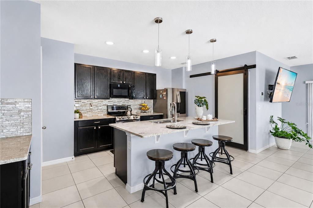 A kitchen features dark cabinets, a granite-topped island with four stools, and light tile flooring — 1795 PARTIN TERRACE ROAD S, KISSIMMEE, FL