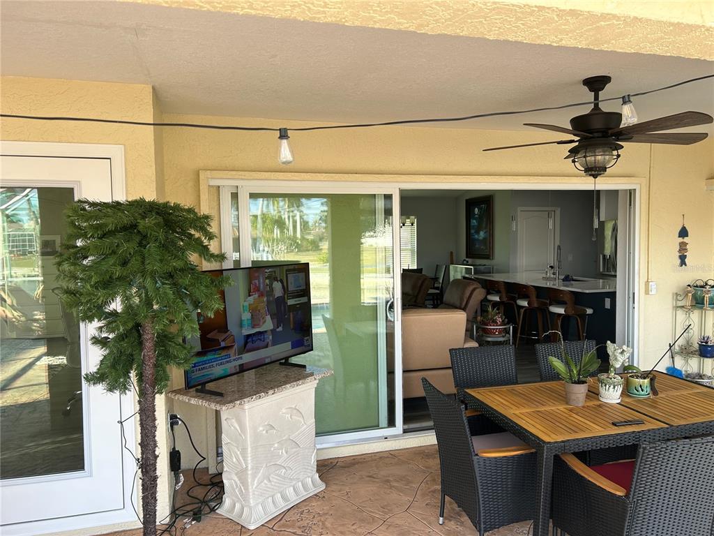A covered patio features a dining set, a television on a pedestal, and sliding glass doors — 1727 BOCA RATON COURT, PUNTA GORDA, FL