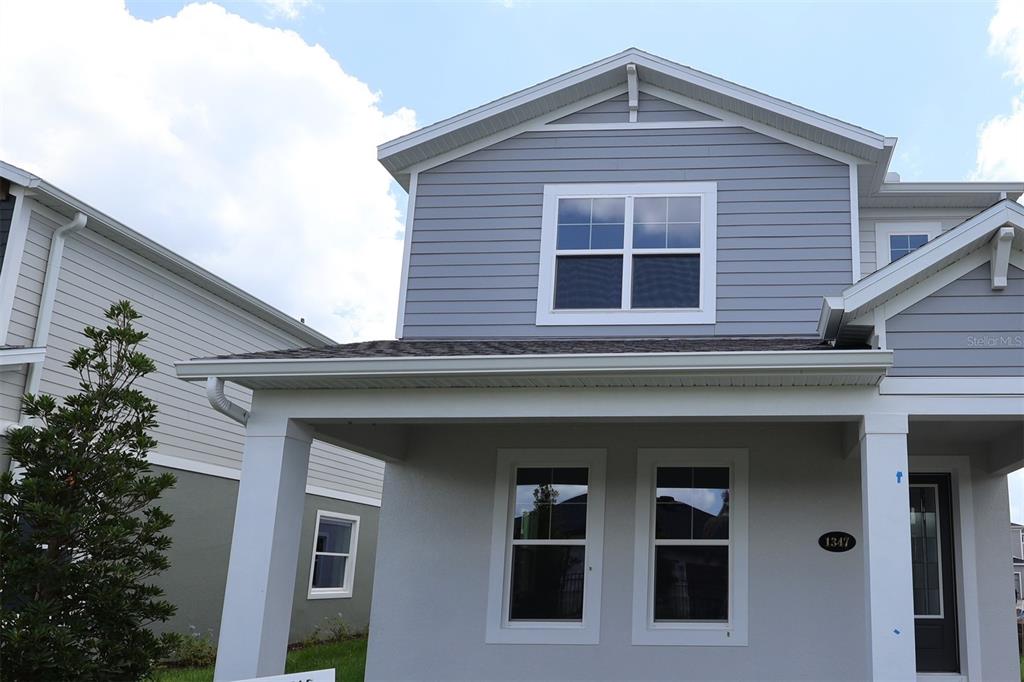 A two-story house with gray siding, a front porch, and white trim under a blue sky — 1347 LUMPINI STREET, ST CLOUD, FL