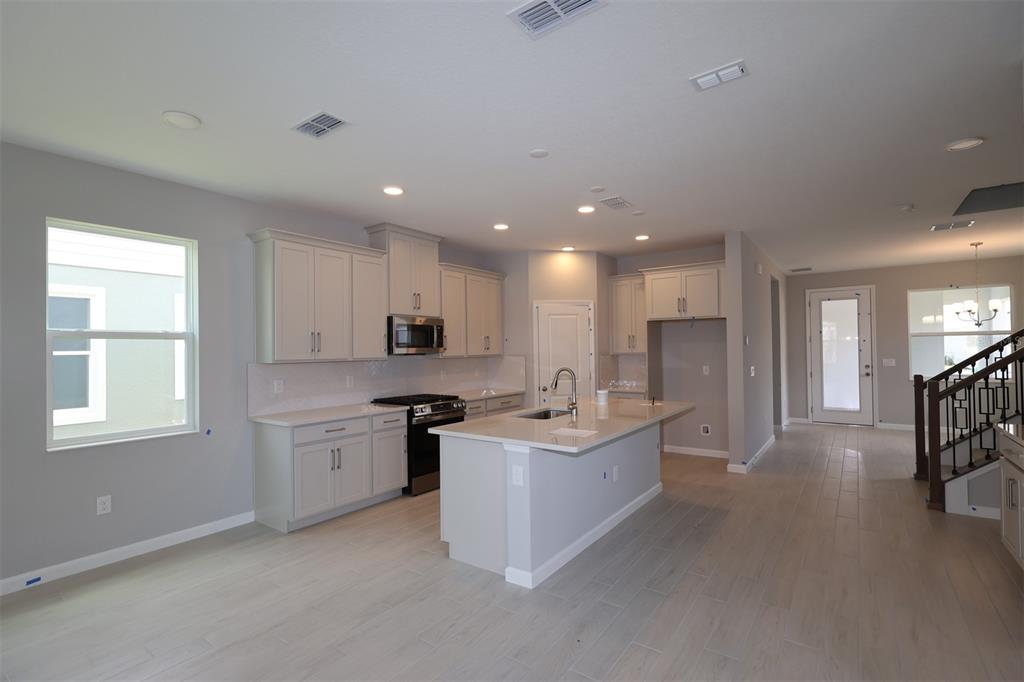A modern kitchen features light gray cabinetry, a central island, and wood-look tile flooring — 1347 LUMPINI STREET, ST CLOUD, FL