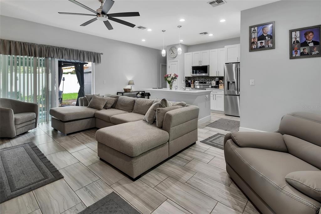 An open-concept living room and kitchen featuring tile flooring, a sectional sofa, and white cabinetry — 1580 13TH STREET, ORANGE CITY, FL