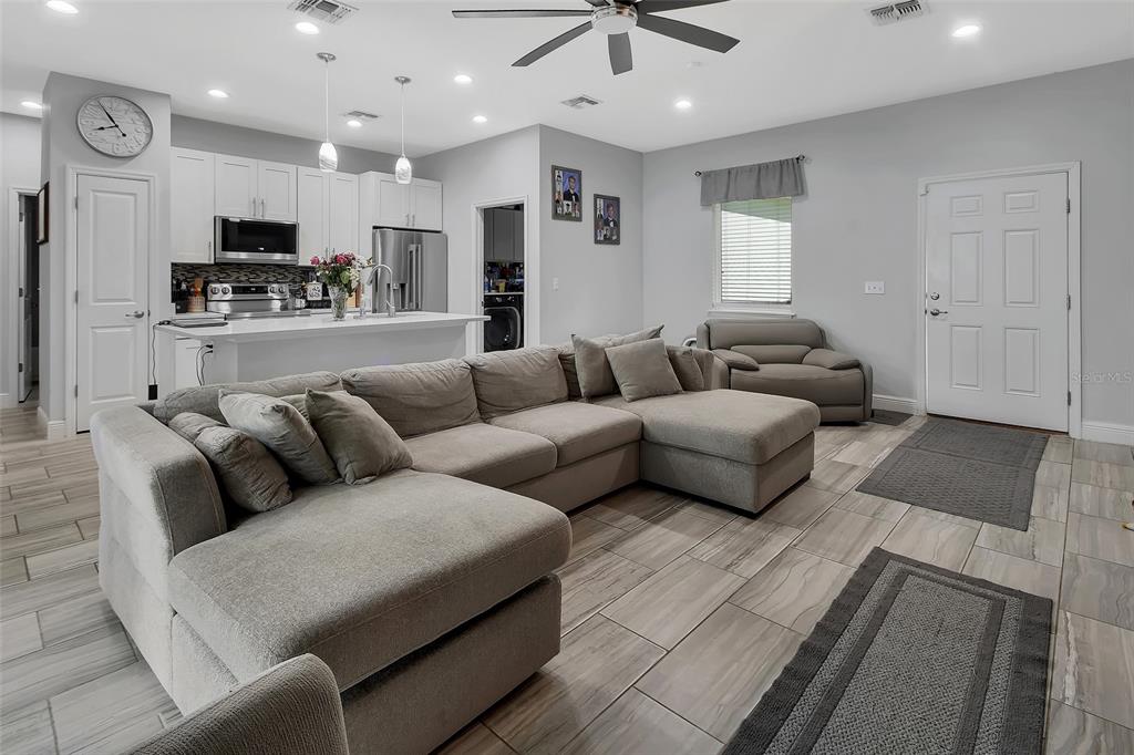 An open-concept living room and kitchen featuring a large gray sectional sofa and tile flooring — 1580 13TH STREET, ORANGE CITY, FL