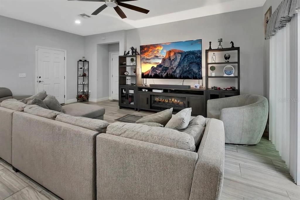 A living room features a large sectional sofa, a fireplace console, and light wood flooring — 1580 13TH STREET, ORANGE CITY, FL