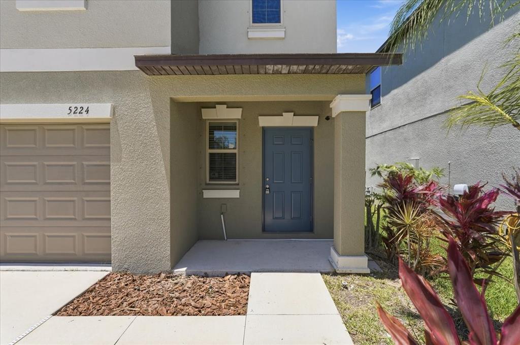 The exterior of a house features a tan stucco facade, a blue front door, and landscaping — 5224 WHITE CHICORY DRIVE, APOLLO BEACH, FL
