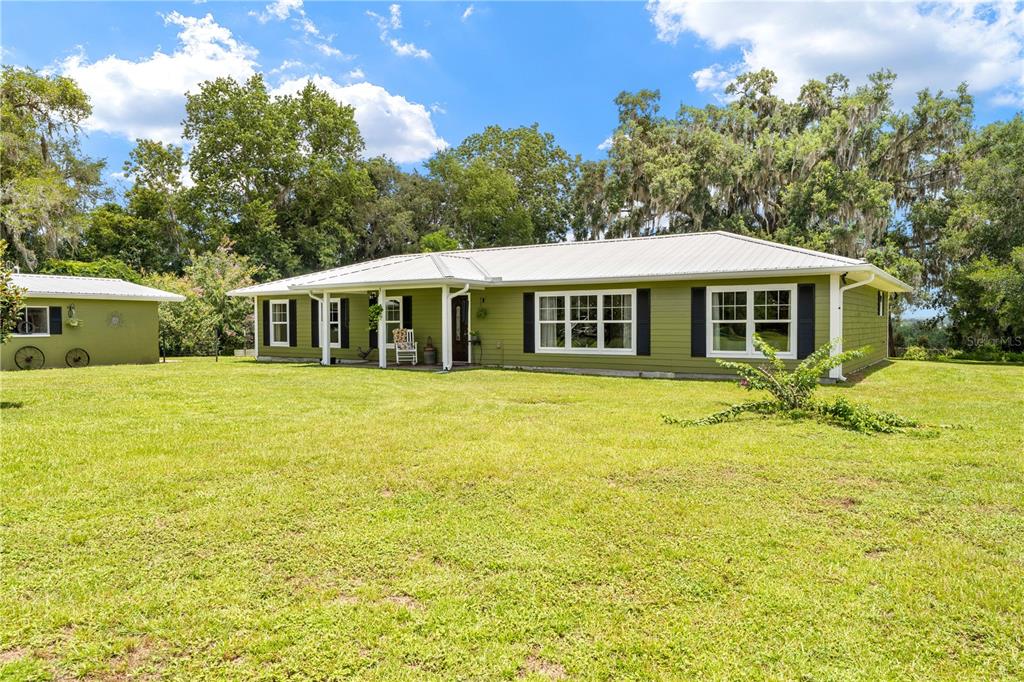 A single-story olive green house with a white metal roof sits on a grassy lawn — 23439 CROOM ROAD, BROOKSVILLE, FL