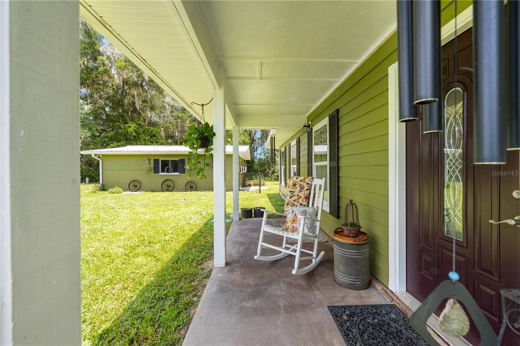 A covered porch with a white rocking chair, green siding, and a dark front door — 23439 CROOM ROAD, BROOKSVILLE, FL