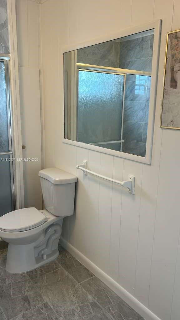 A bathroom features a white toilet, a wall-mounted mirror, and white vertical wood paneling — 1911 SW 87th Ave, Davie FL 33324, DAVIE, FL