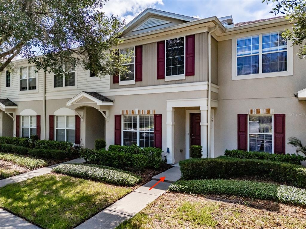 A two-story townhouse exterior features beige siding, maroon shutters, and a concrete walkway — 15911 FISHHAWK VIEW DRIVE, LITHIA, FL