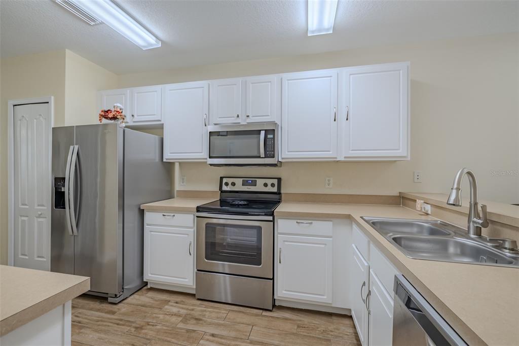 A kitchen features white cabinets, stainless steel appliances, and light-colored countertops — 15911 FISHHAWK VIEW DRIVE, LITHIA, FL