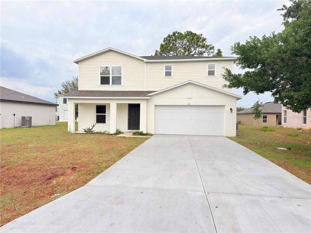 A two-story house with beige siding, a front porch, and an attached two-car garage — 733 JAMES COURT, KISSIMMEE, FL