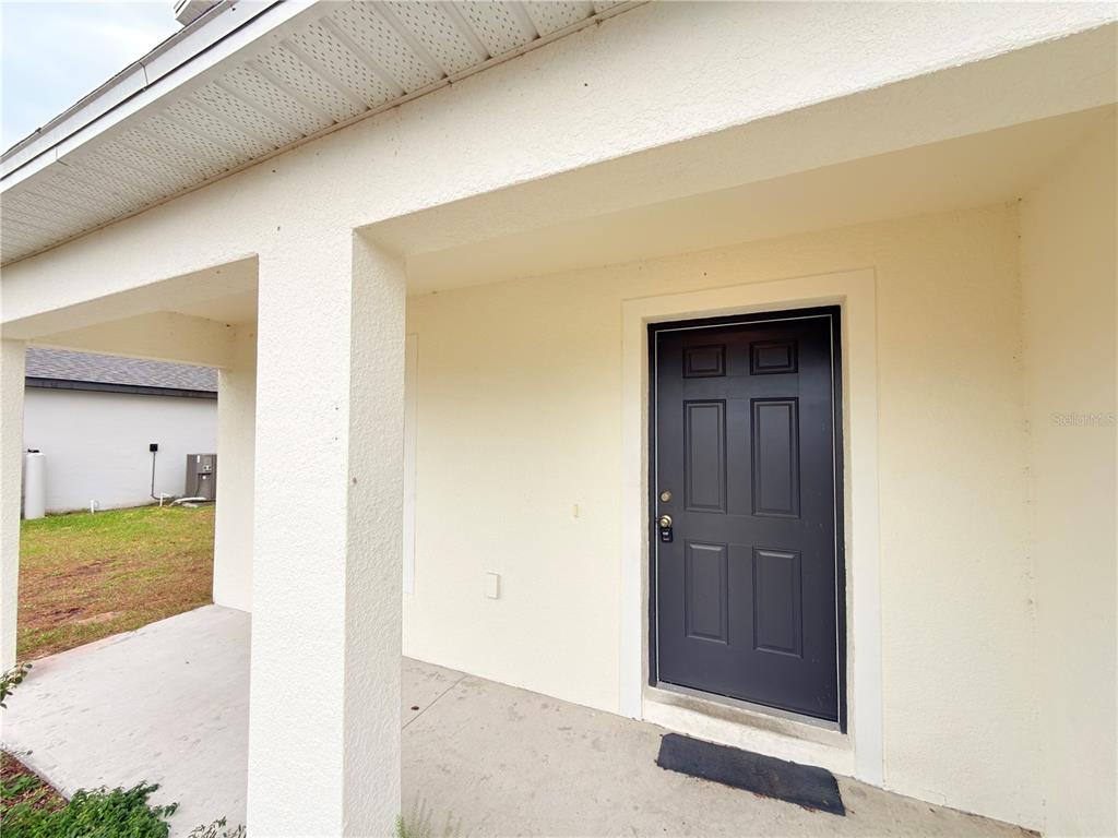 A covered concrete porch leads to a dark gray front door on a stucco house — 733 JAMES COURT, KISSIMMEE, FL