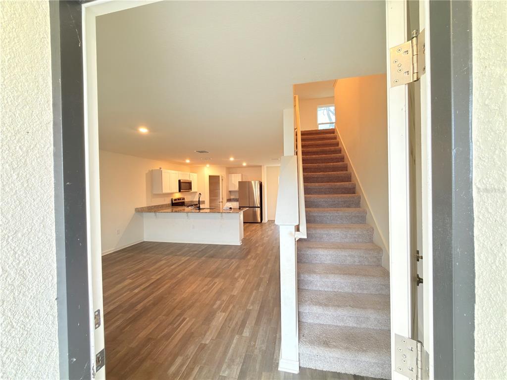 A view from a doorway shows a carpeted staircase next to an open-concept kitchen area — 733 JAMES COURT, KISSIMMEE, FL