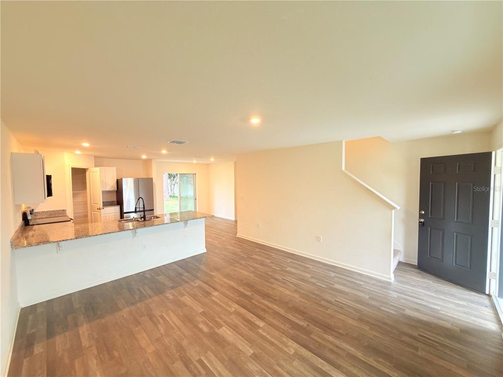 An open-concept living area features wood-look flooring, a kitchen with granite countertops, and stairs — 733 JAMES COURT, KISSIMMEE, FL
