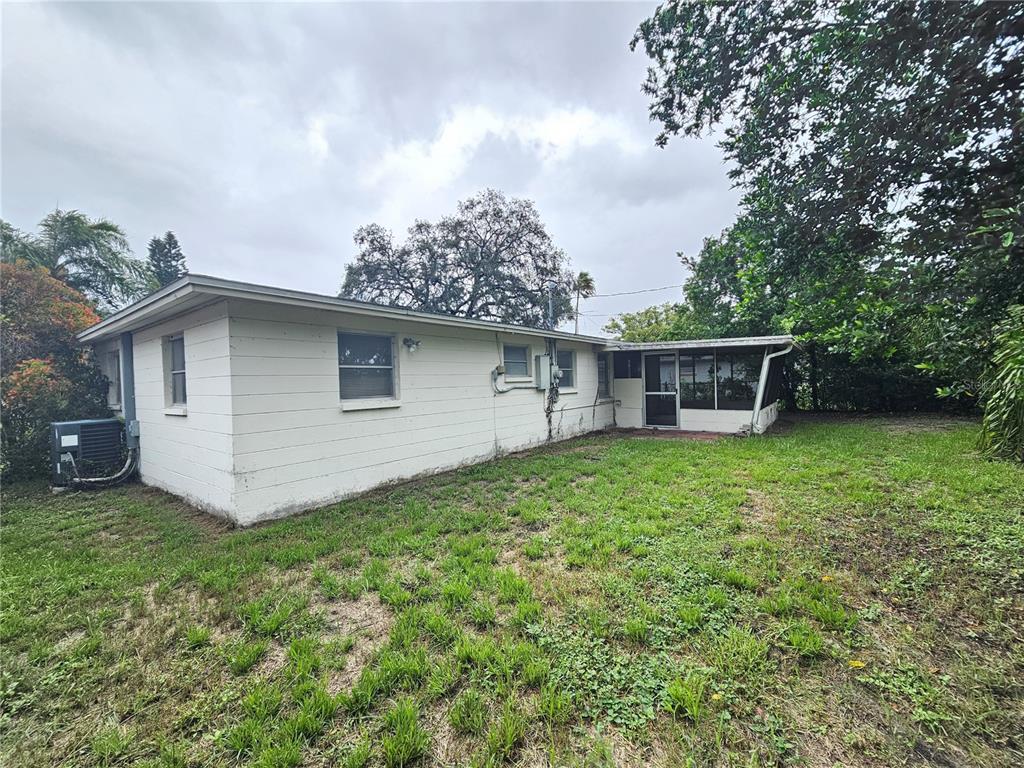 The exterior of a white, single-story house with a screened-in porch and a grassy yard — 1702 AQUA LANE, HOLIDAY, FL