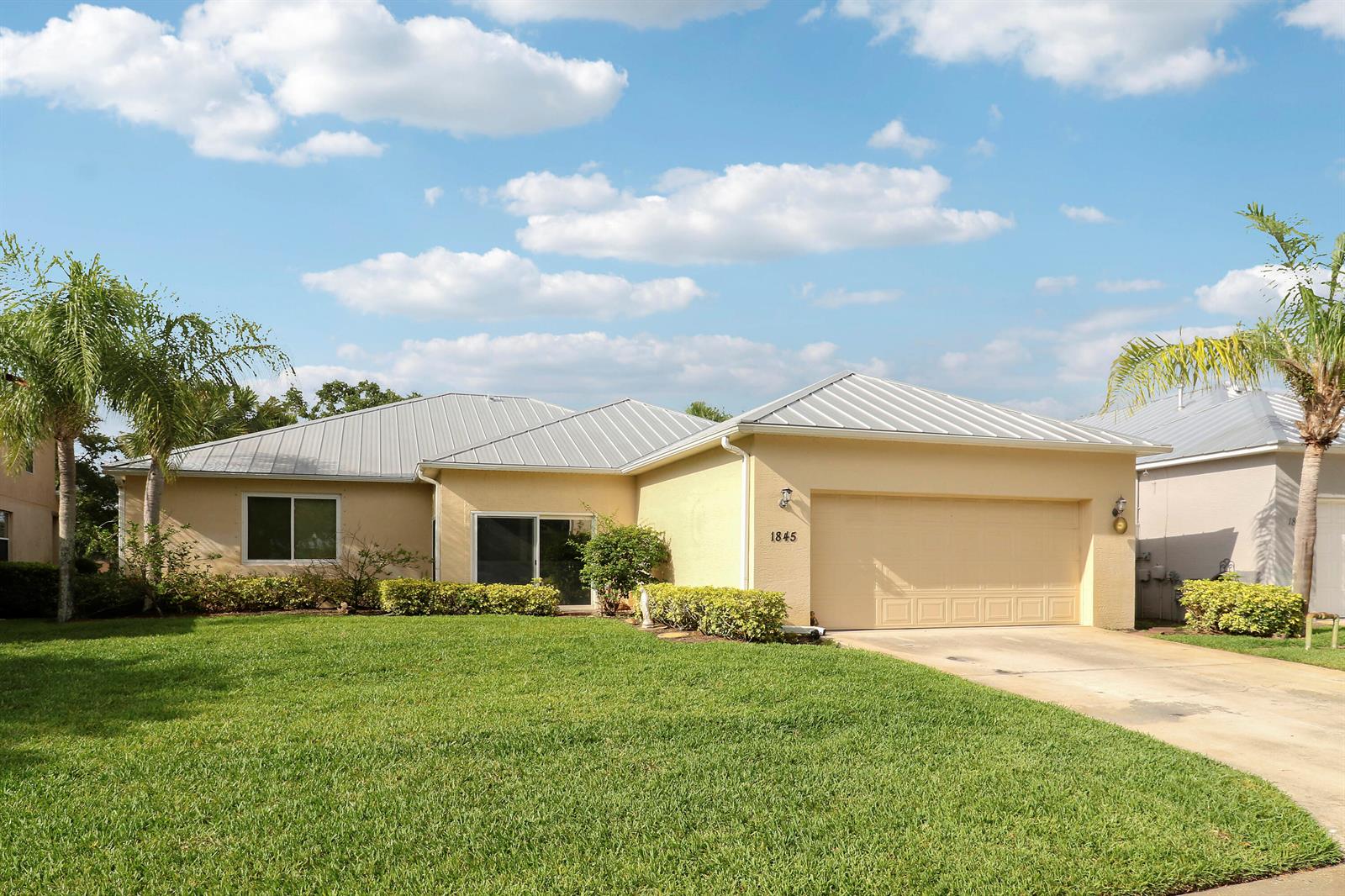 A single-story house with a yellow stucco exterior, metal roof, and attached two-car garage — 1845 Pointe West Way, Vero Beach FL 32966, VERO BEACH, FL