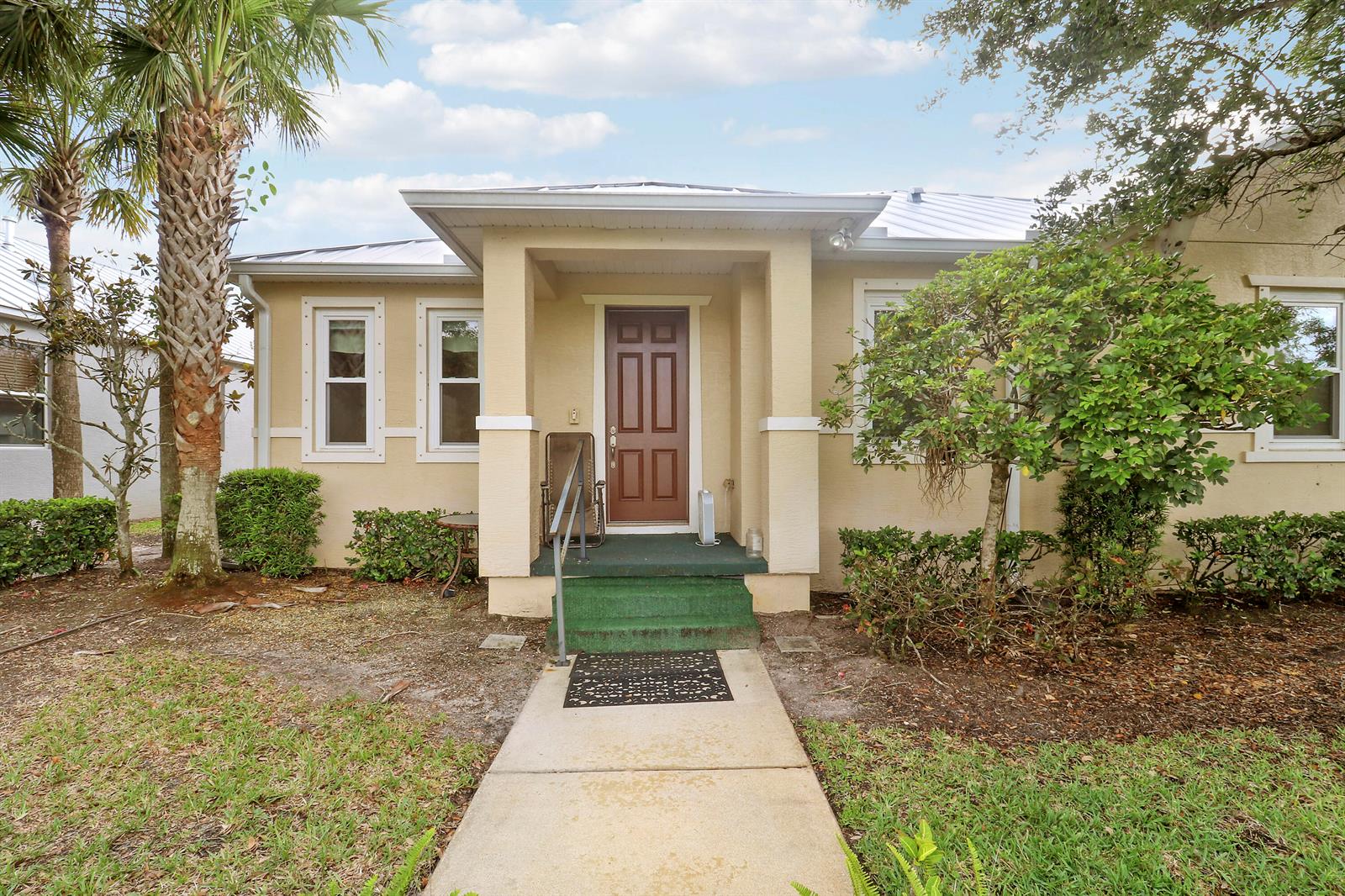 A tan house exterior features a brown front door, a concrete walkway, and landscaping — 1845 Pointe West Way, Vero Beach FL 32966, VERO BEACH, FL