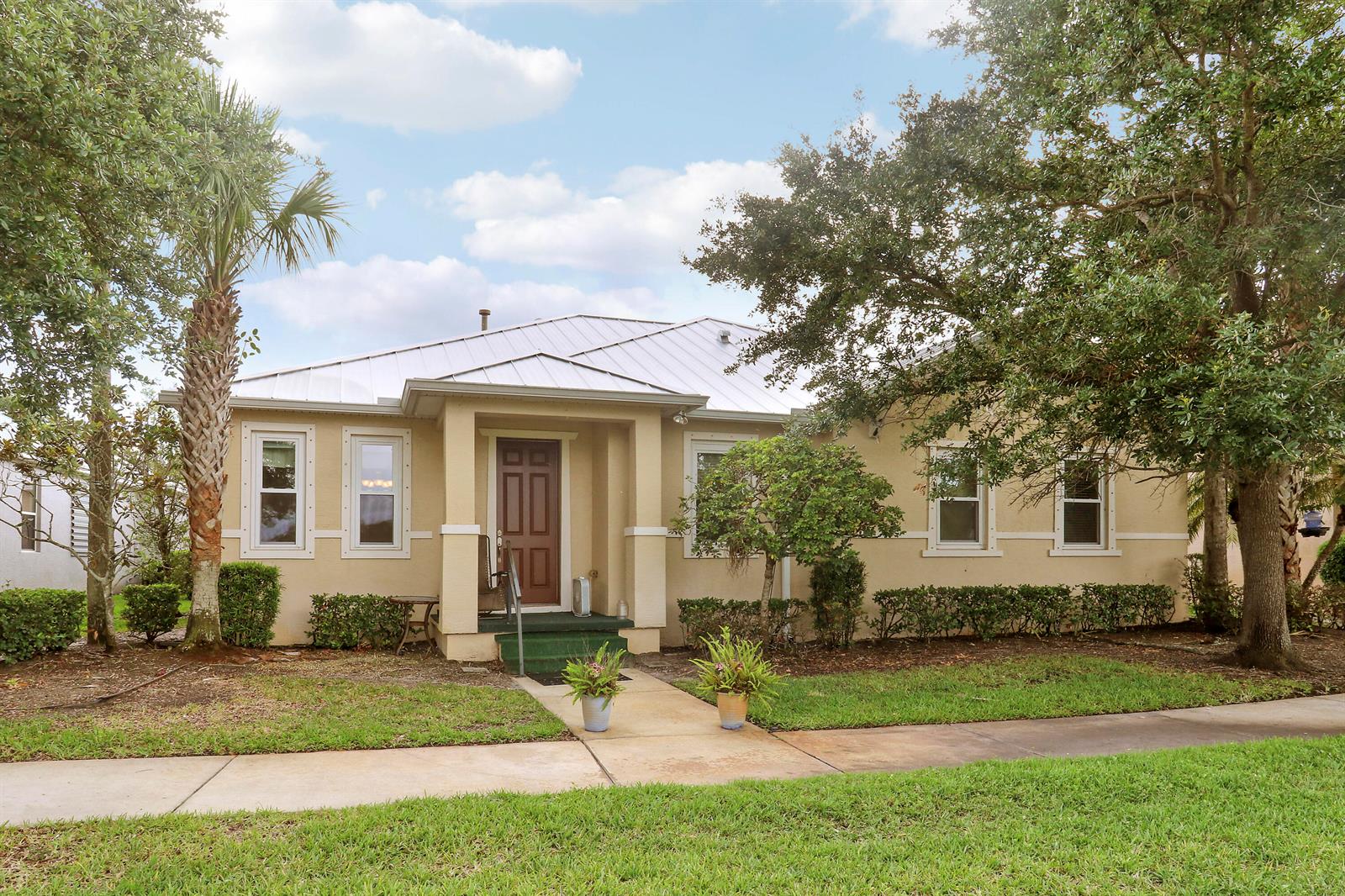 A single-story tan house with a metal roof and a front porch sits behind a lawn — 1845 Pointe West Way, Vero Beach FL 32966, VERO BEACH, FL