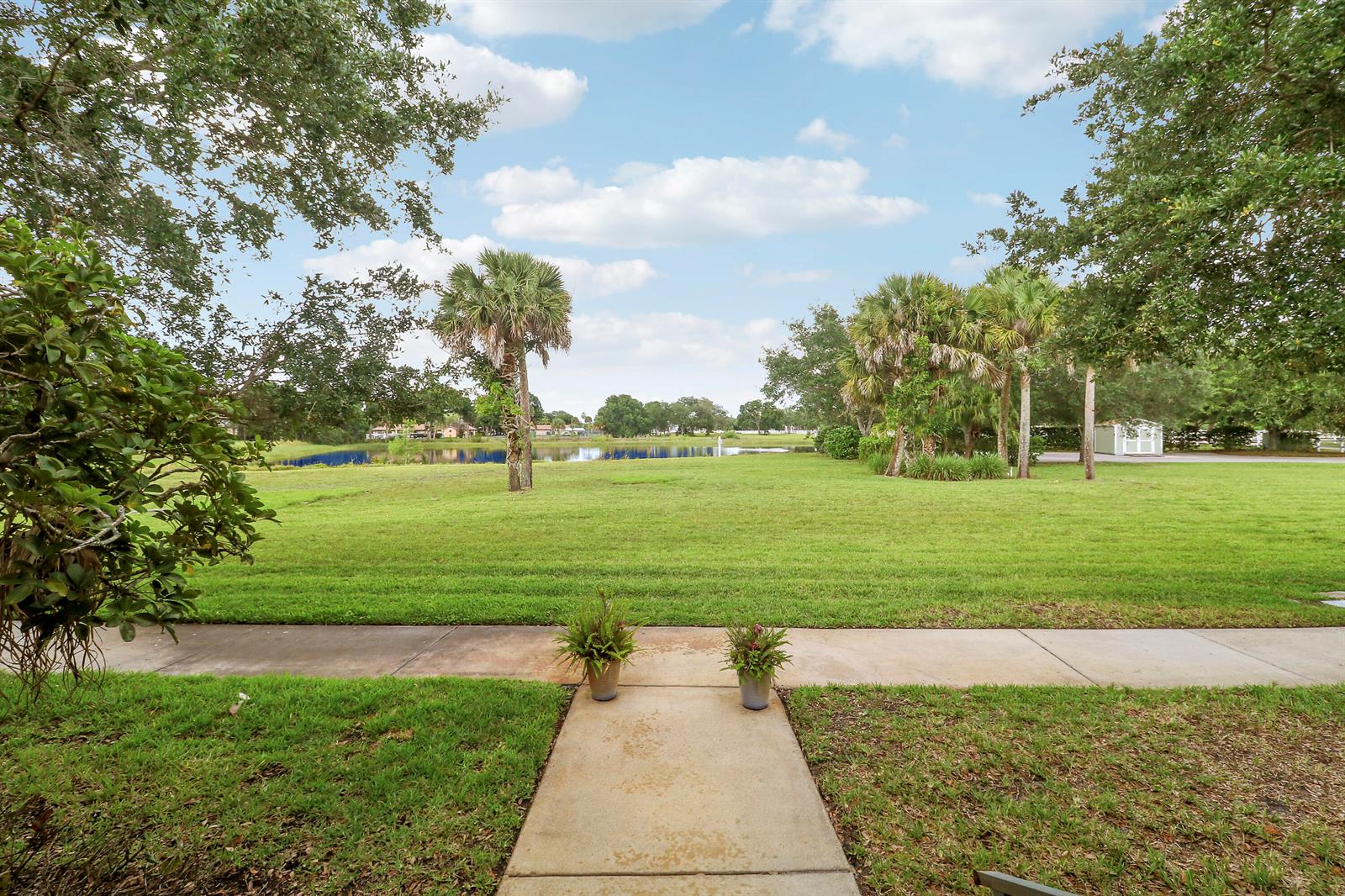 A concrete walkway leads through a grassy yard toward a pond and palm trees — 1845 Pointe West Way, Vero Beach FL 32966, VERO BEACH, FL