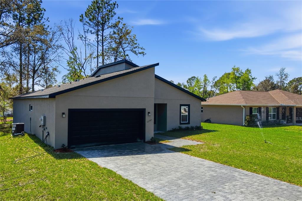A modern, single-story house with a black garage door and a paved driveway — 12797 SW 58TH CIRCLE, OCALA, FL