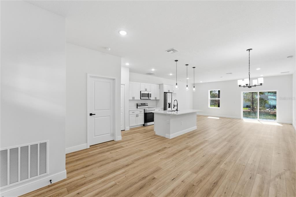 A modern kitchen with white cabinets and an island opens into a spacious living area — 12797 SW 58TH CIRCLE, OCALA, FL