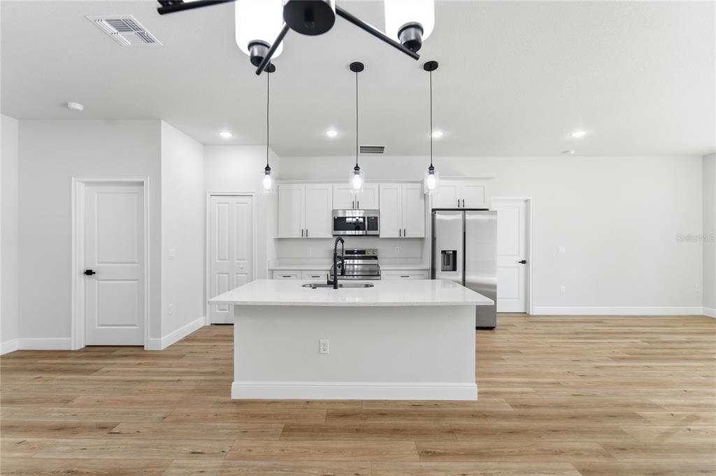 A modern kitchen features white cabinetry, stainless steel appliances, a central island, and wood flooring — 12797 SW 58TH CIRCLE, OCALA, FL