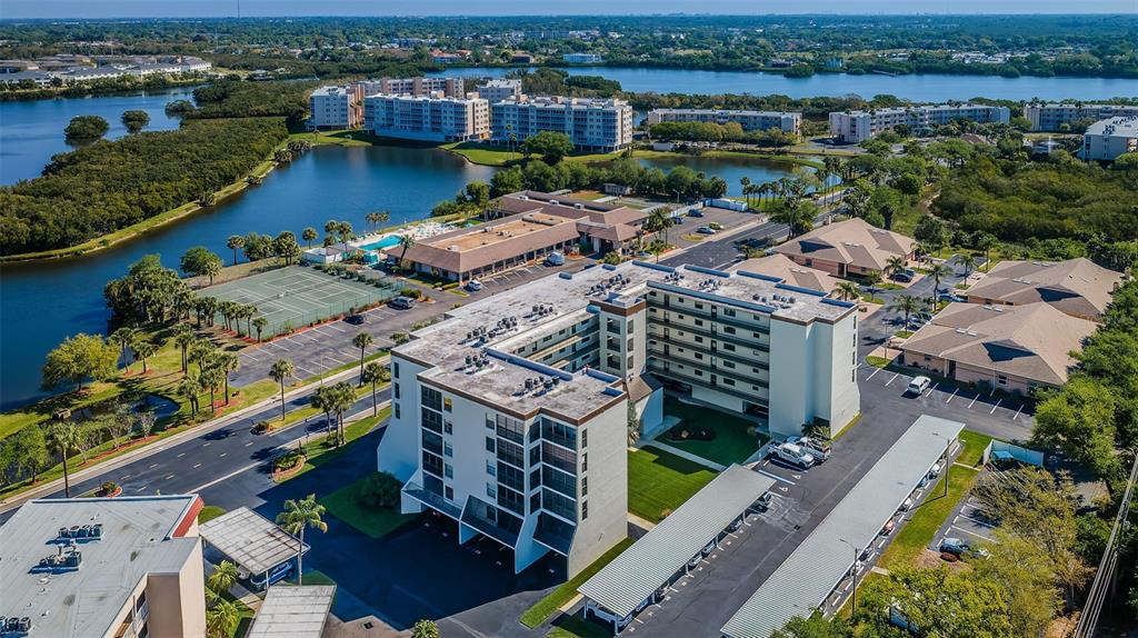 An aerial view shows a multi-story apartment complex surrounded by parking lots, trees, and water — 9860 62ND TERRACE N UNIT 1025, ST PETERSBURG, FL