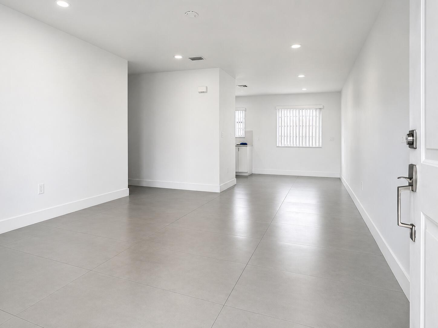 An empty room with white walls, gray tile flooring, and a view of a kitchen — 2152 SW 72nd Avenue, Miami FL 33155, MIAMI, FL