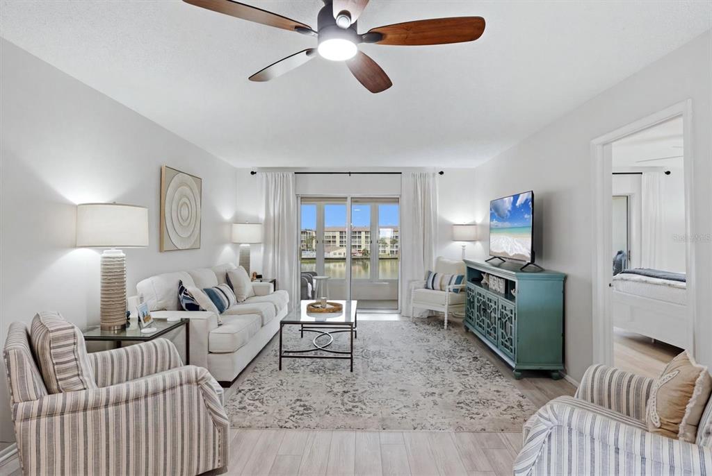 A living room features a sofa, two striped armchairs, a television, and a sliding glass door — 3446 LAKE BAYSHORE DRIVE UNIT 416, BRADENTON, FL