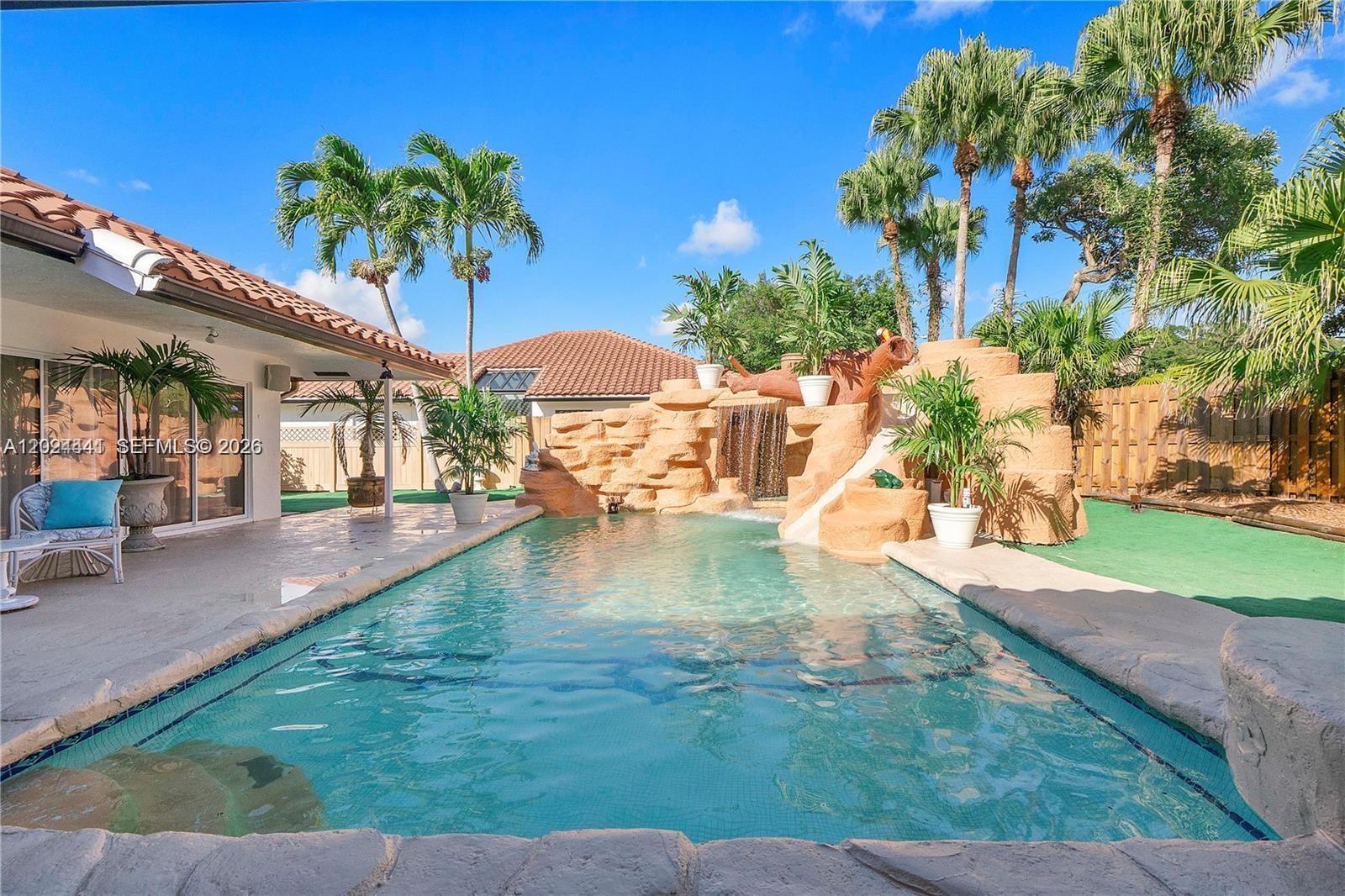 A backyard swimming pool features a rock waterfall and slide with surrounding palm trees — 2900 NW 25th Way, Boca Raton FL 33434, BOCA RATON, FL