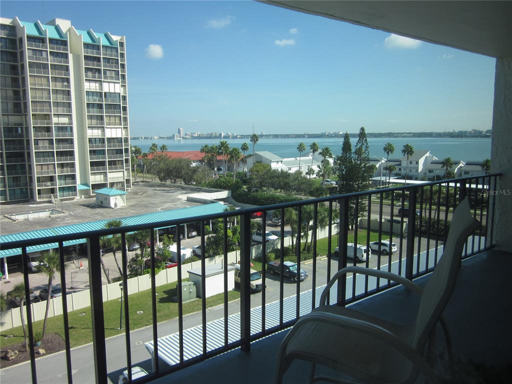 A balcony view overlooks a parking lot, palm trees, and a large body of water — 1400 GULF BOULEVARD UNIT 608, CLEARWATER BEACH, FL
