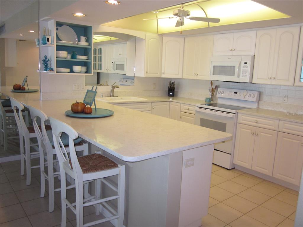 A kitchen features white cabinets, a large island with bar seating, and light-colored countertops — 1400 GULF BOULEVARD UNIT 608, CLEARWATER BEACH, FL