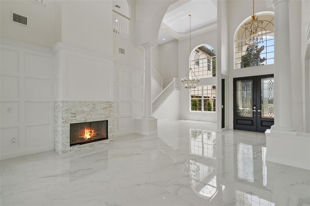 A bright, high-ceilinged living room features white marble floors, a stone fireplace, and a staircase — 408 CHELSEA AVENUE, DAVENPORT, FL