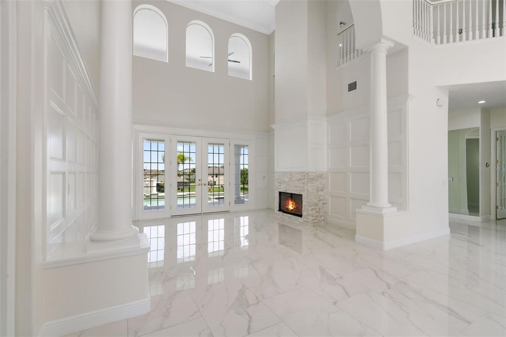 A bright living room features white marble floors, a stone fireplace, and tall arched windows — 408 CHELSEA AVENUE, DAVENPORT, FL
