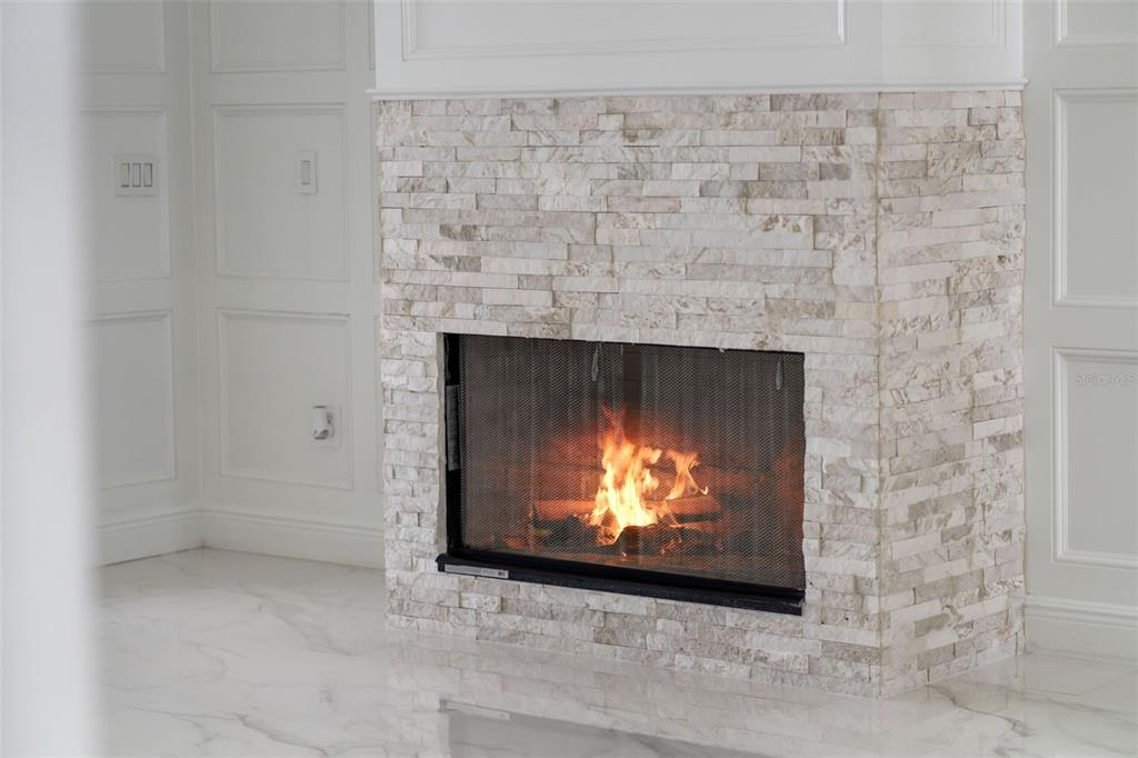 A fireplace with a light-colored stacked stone surround sits in a room with white paneling — 408 CHELSEA AVENUE, DAVENPORT, FL