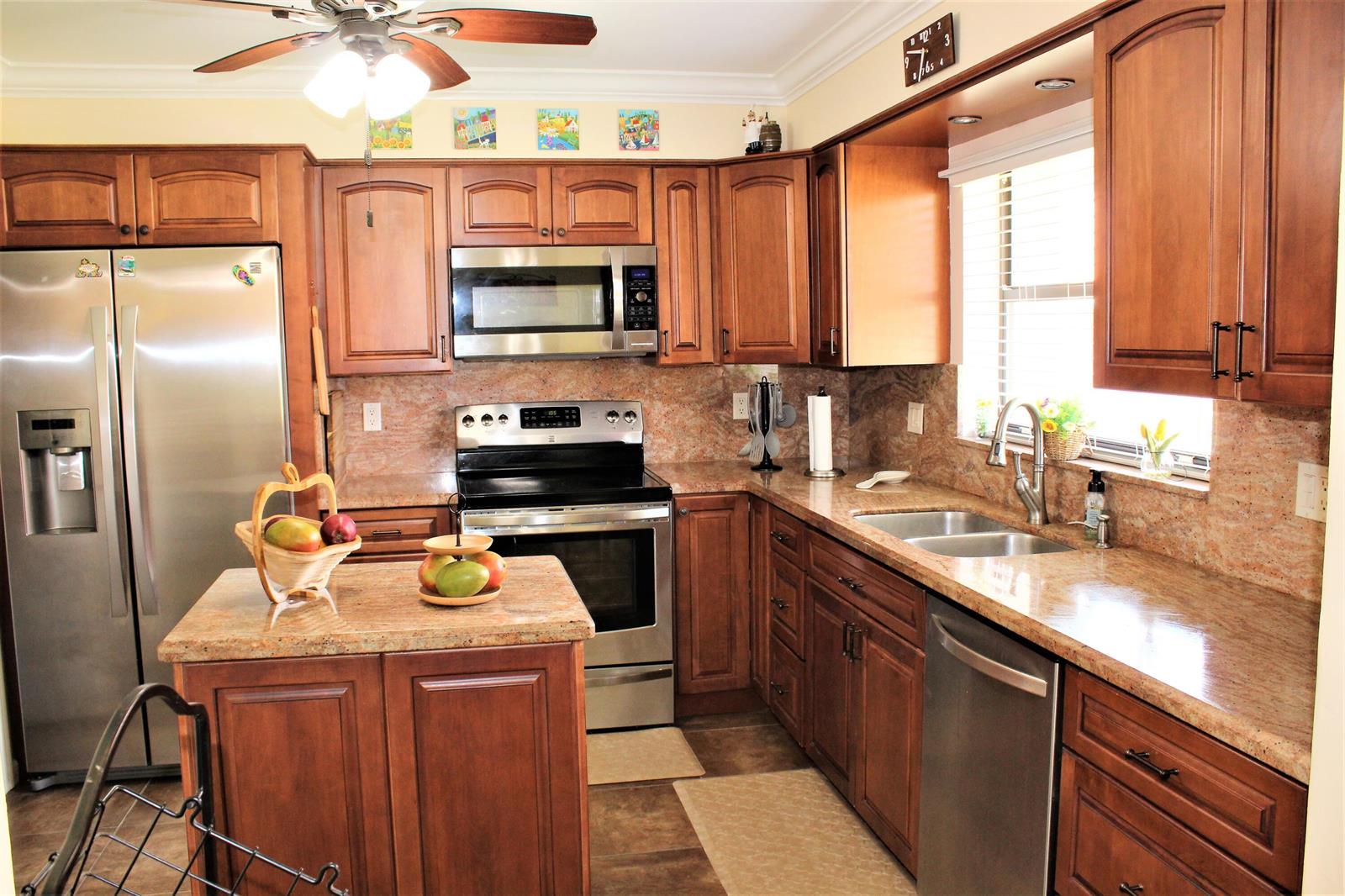 A kitchen with wood cabinets, granite countertops, stainless steel appliances, and a central island — 9940 Bauhinia Tree Way # B, Boynton Beach FL 33436, BOYNTON BEACH, FL