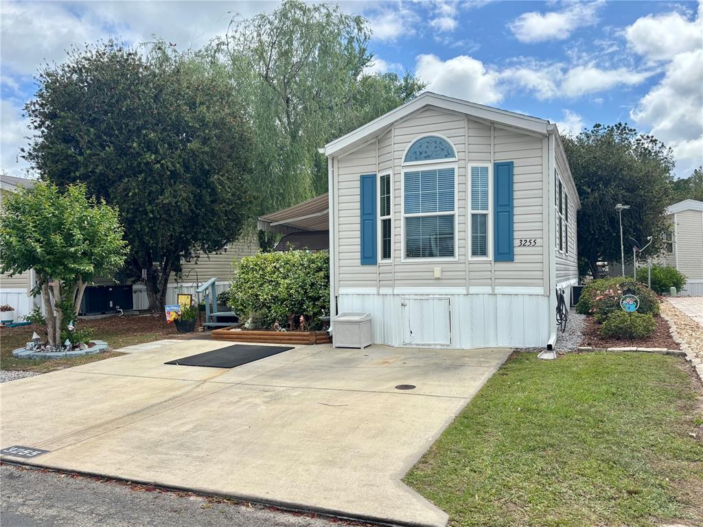 A beige manufactured home with blue shutters and a concrete driveway sits on a lot — 3255 NE 104TH AVENUE, SILVER SPRINGS, FL
